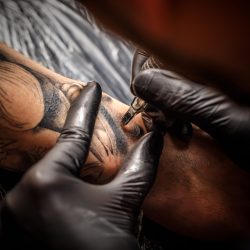 Hands of the artist tattooing of man's skin