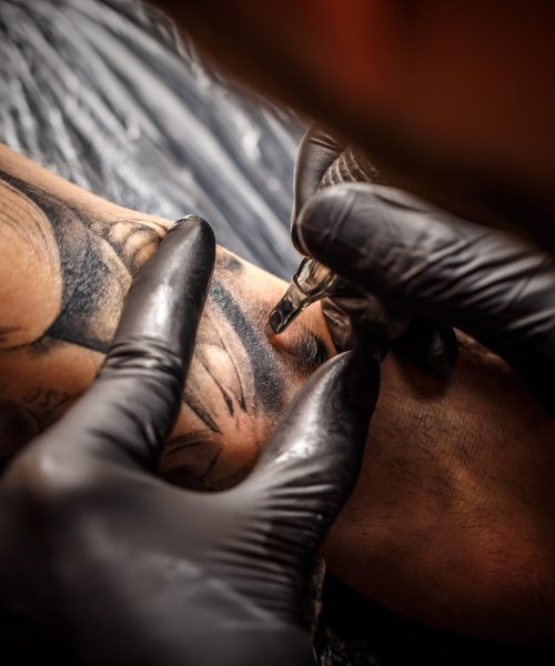 Hands of the artist tattooing of man's skin