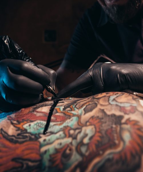 Cropped shot of an artist hands in a protective gloves holding ma machine while the ink is dropping