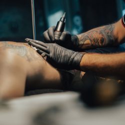 Professional tattoo artist making a tattoo on a man skin while working in a dark tattoo studio. Tattooing. Concept of art and design.