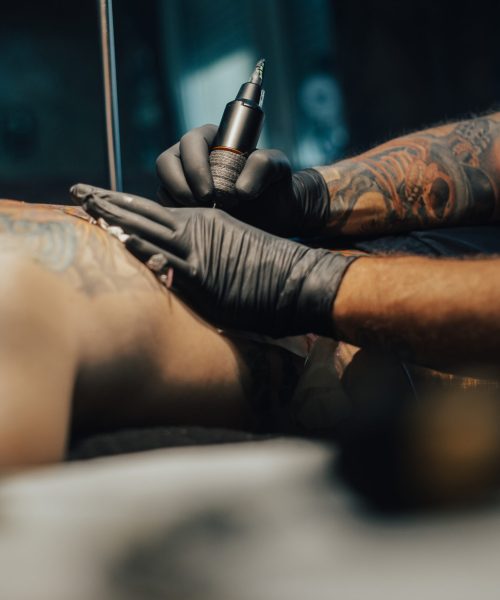 Professional tattoo artist making a tattoo on a man skin while working in a dark tattoo studio. Tattooing. Concept of art and design.