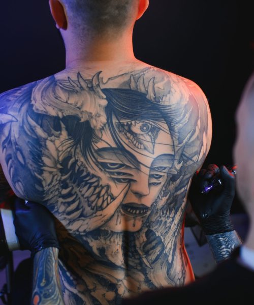 Tattooing. Man creating a picture on his back by a professional tattoo artist.